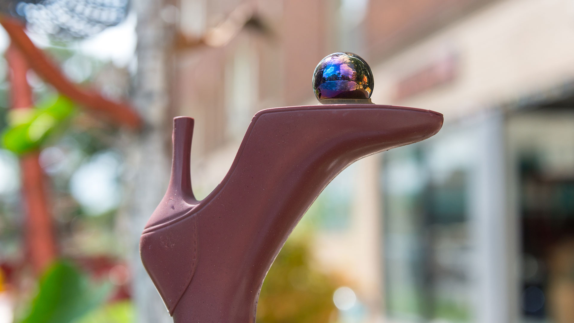 Close-up of a sculptural art piece shaped like a high-heeled shoe with a reflective marble on top, located in the Oak Park Arts District.