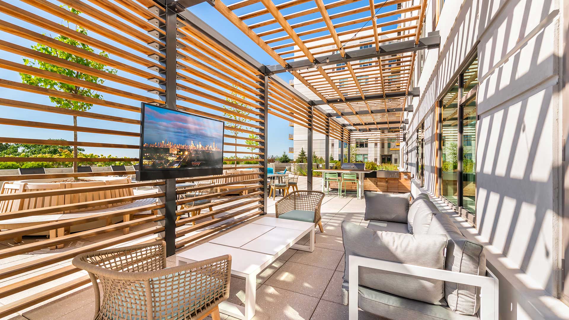 Outdoor lounge at Eleven33 Apartments in Oak Park featuring shaded pergola, modern seating, TV, and grilling area.