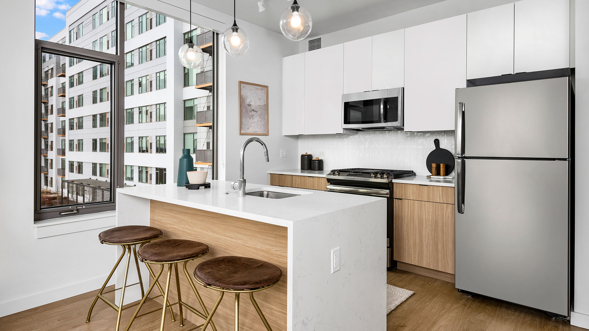 Modern kitchen at Eleven33 Apartments in Oak Park featuring quartz island with seating, stainless steel appliances, and contemporary pendant lighting.
