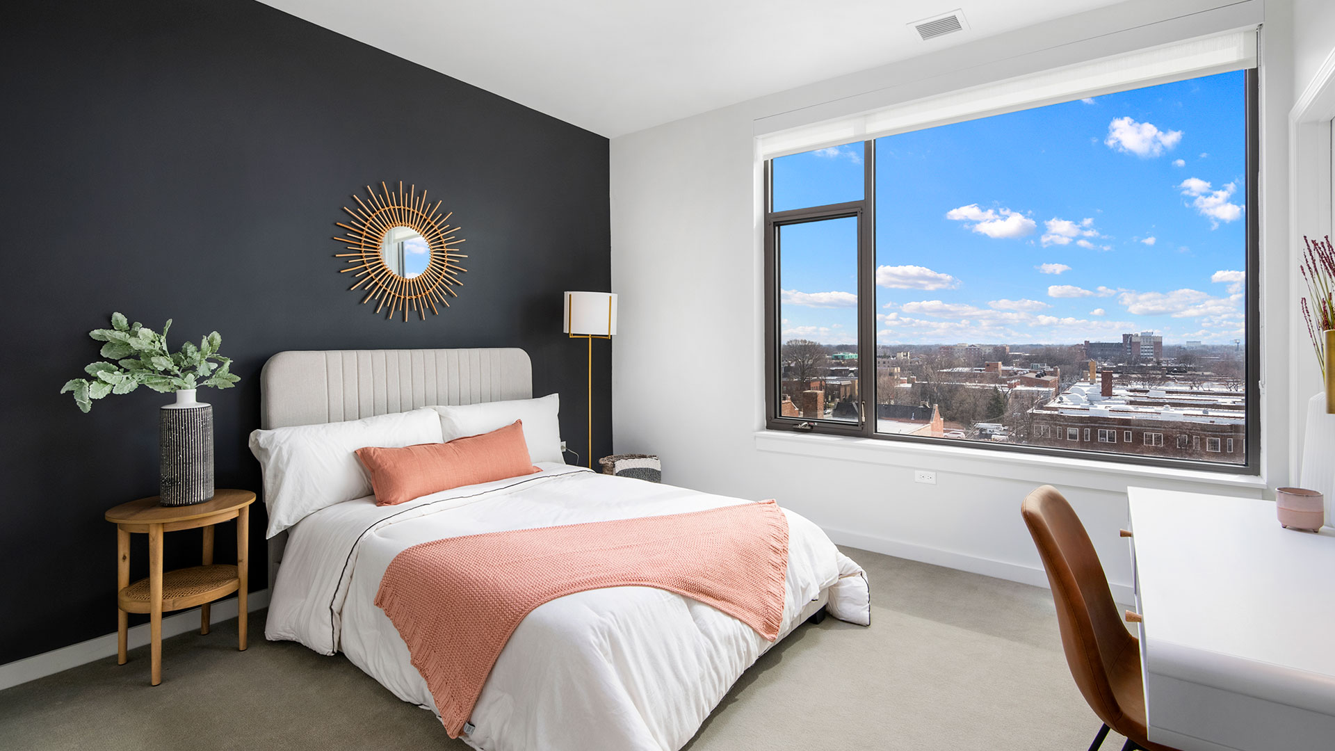 Modern bedroom at Eleven33 Apartments in Oak Park featuring dark accent wall, large window with skyline view, and contemporary decor.