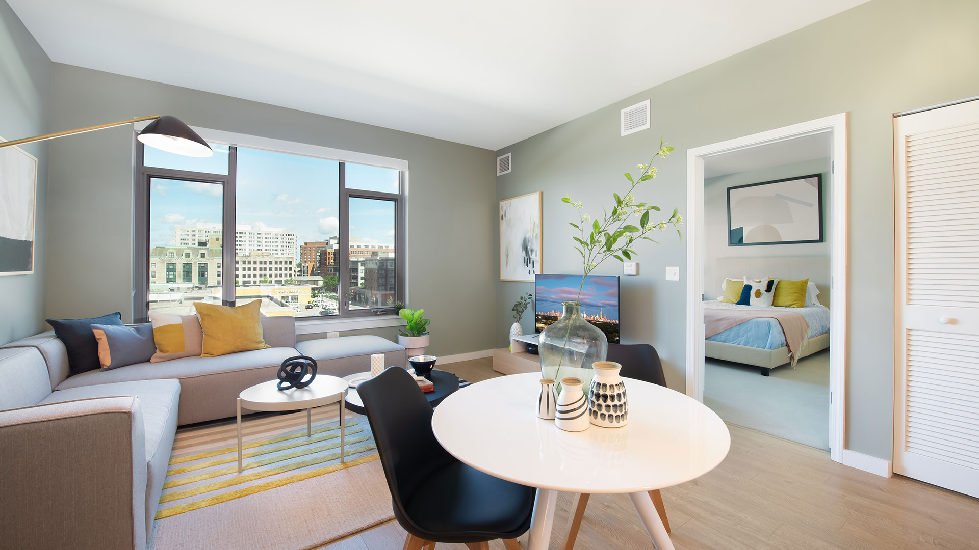 Open living room and bedroom at Eleven33 Apartments in Oak Park featuring large windows, modern furniture, and soft natural light.