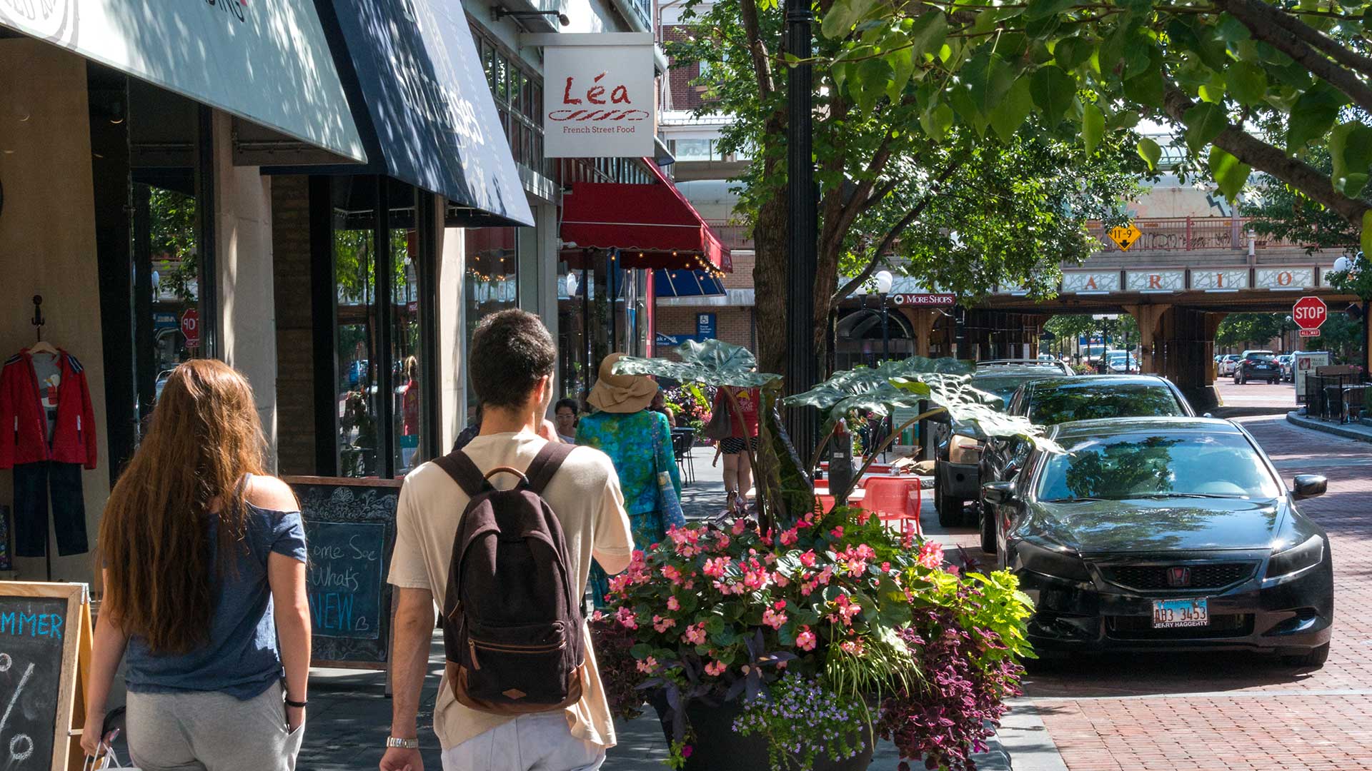 People walking along a tree-lined street in downtown Oak Park near cafés and local shops, with planters and storefronts creating a lively, welcoming atmosphere.